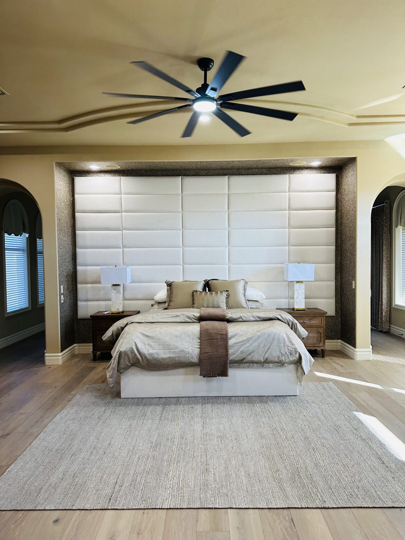 Neutral master bedroom with padded headboard, ceiling fan